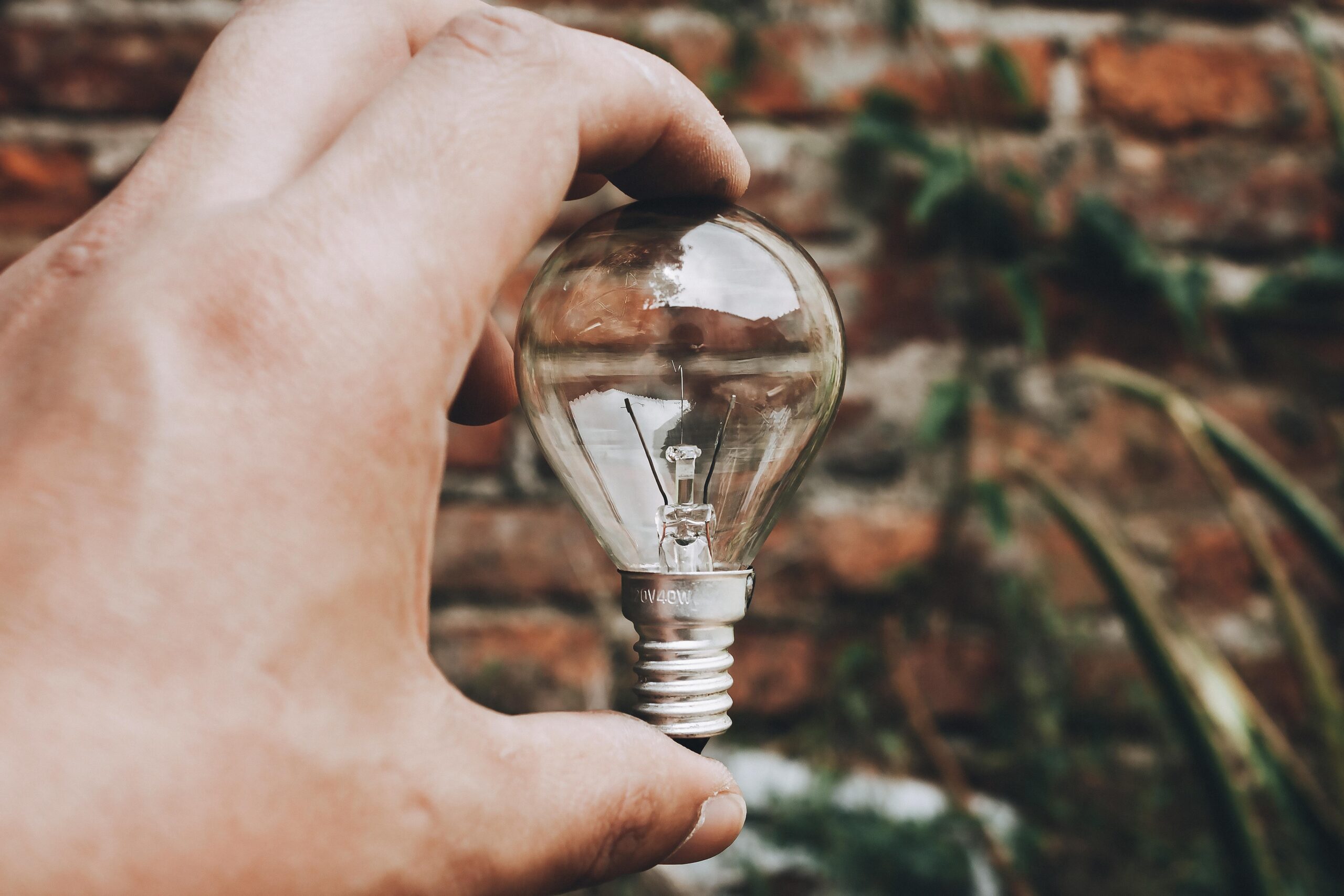Close-up of hand holding a clear light bulb with a brick wall background, capturing innovative and eco-friendly themes.